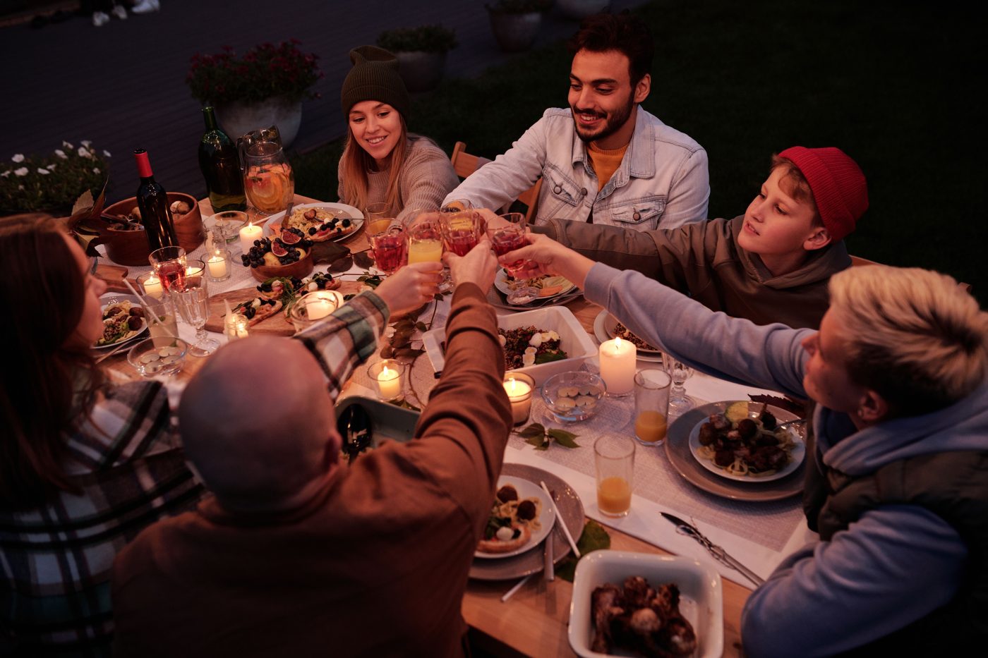 Freunde stoßen abends an einem Gartentisch mit Kerzen und vielen Schüsseln an.